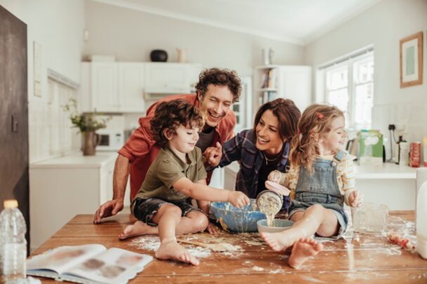 Joyful mother and father looking at young son and daughter in kitchen while mixing ingredients in a bowl