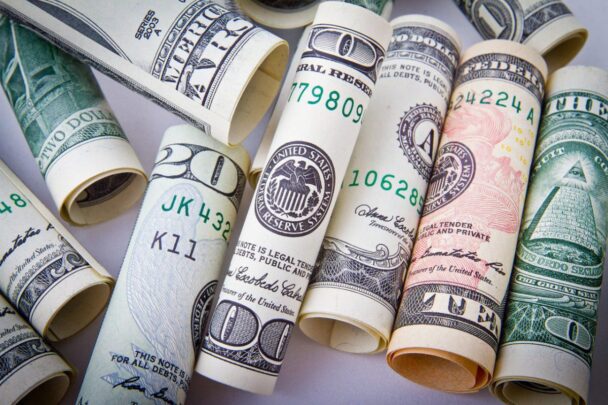 various US currency rolled tightly and lined up together, including a twenty and one hundred dollar bill