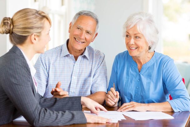older couple smiling and speaking to a woman wearing a suit while pointing to papers on the table in front of them