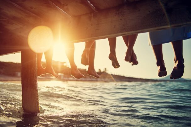 feet dangling from a dock above the ocean at sunset