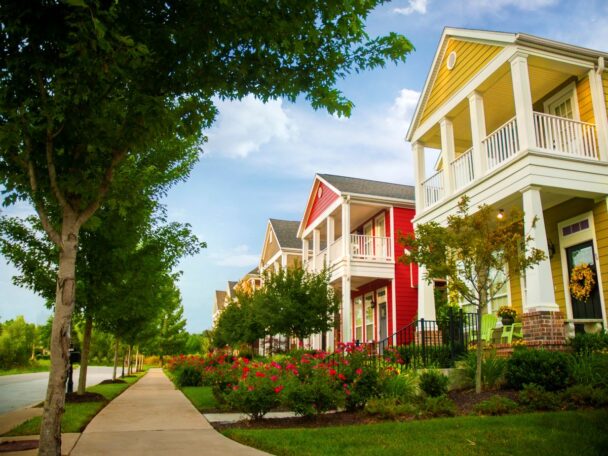 row of colorful shotgun style houses on tree lined street in afternoon sunlight