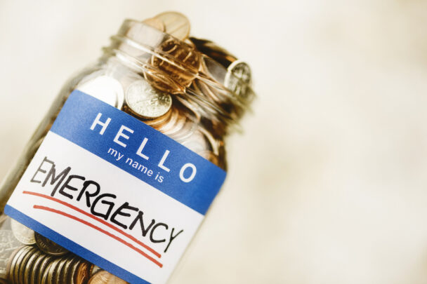 overturned mason jar overfilled with coins with a sticker that reads "hello, my name is emergency"