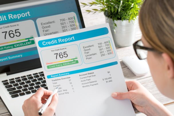 woman wearing glasses looking down at a paper showing a credit report with a credit score of 765